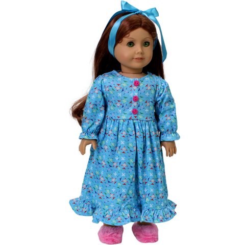 An 18-inch doll wearing a blue nightgown with a airplane print and a blue satin hair ribbon.