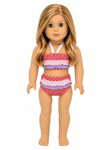 An 18-inch doll wearing a two-piece swimsuit with red and white polka-dot ruffles and purple and white striped ruffles, shown against a plain white background.